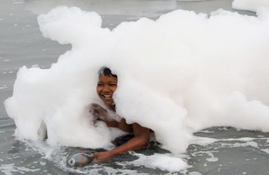 A child fills a bottle with water while bathing in the polluted waters of the river Yamuna on a smoggy morning in New Delhi